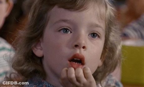 A Little Girl Is Sitting In A Classroom With Her Mouth Open And Her Hands On Her Face . GIF