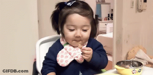 A Little Girl Is Sitting In A High Chair Eating A Piece Of Food . GIF