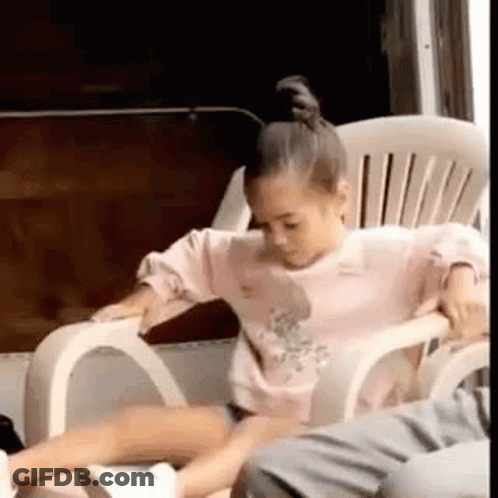 A Little Girl Is Sitting In A White Chair . GIF