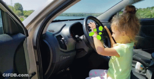 A Little Girl Is Sitting In The Driver 'S Seat Of A Car Playing With The Steering Wheel GIF