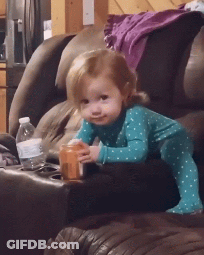 A Little Girl Is Sitting On A Couch Holding A Bottle Of Water GIF