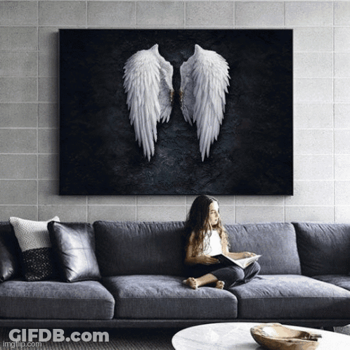 A Little Girl Is Sitting On A Couch Reading A Book Under A Painting Of Angel Wings GIF