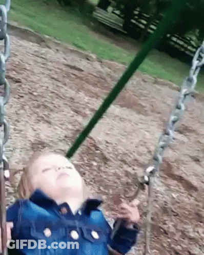A Little Girl Is Sitting On A Swing In A Park With Her Eyes Closed . GIF