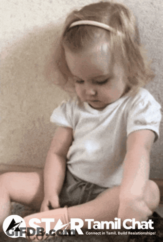 A Little Girl Is Sitting On The Floor With A Star Tamil Chat Logo In The Background GIF