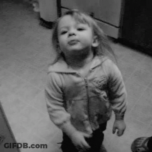 A Little Girl Is Standing In A Kitchen And Making A Funny Face In A Black And White Photo . GIF