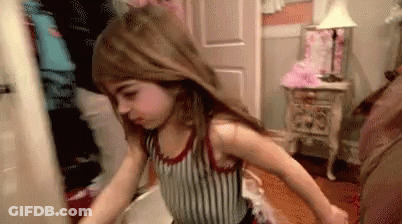 A Little Girl Is Standing In A Room With Her Hair In The Air . GIF