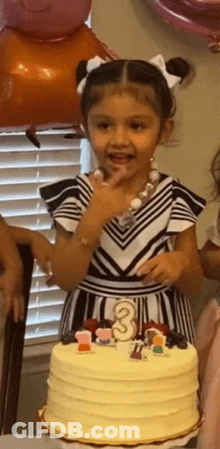 A Little Girl Is Standing In Front Of A Cake That Has The Number 3 On It GIF