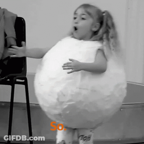 A Little Girl Is Standing In Front Of A Chair Wearing A Costume That Looks Like A Balloon With The Word So On It GIF