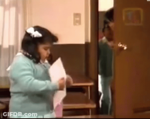 A Little Girl Is Standing In Front Of A Door Holding A Piece Of Paper .. GIF