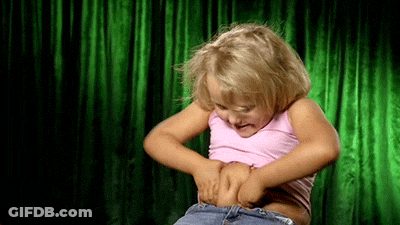 Girl Standing In Front Of Green Curtain Holding Stomach GIF
