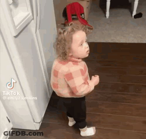 A Little Girl Is Standing In Front Of A Refrigerator And Making A Funny Face . GIF
