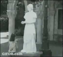 A Little Girl Is Standing In Front Of A Statue Of A Woman In A White Dress . GIF