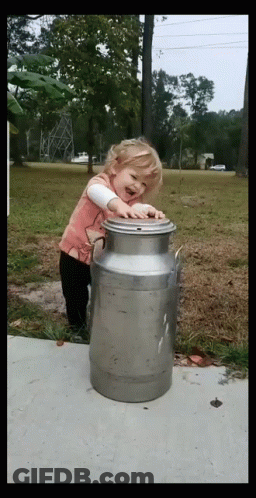 A Little Girl Is Standing Next To A Large Metal Can GIF