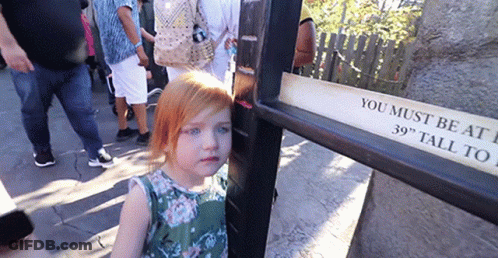 A Little Girl Is Standing Next To A Sign That Says You Must Be At 39 Inches Tall GIF