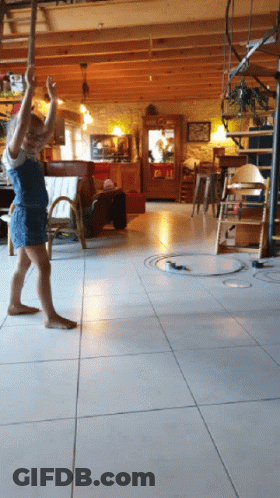 A Little Girl Is Standing On A Tiled Floor In A Living Room With A Spiral Staircase In The Background GIF
