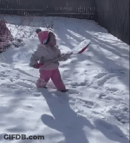 A Little Girl Is Walking Through The Snow While Holding A Shovel . GIF