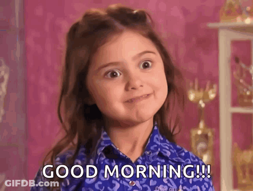 A Little Girl Is Wearing A Blue Shirt And Making A Face And Saying Good Morning . GIF