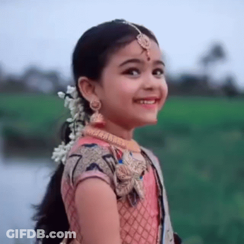 A Little Girl Is Wearing A Pink Dress And Smiling . GIF