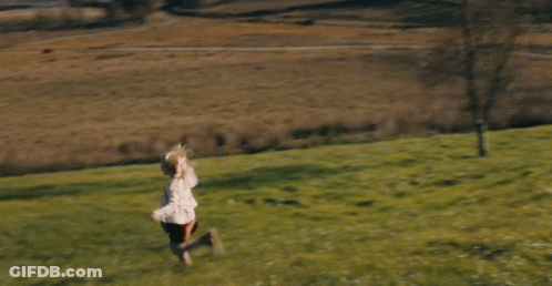 A Little Girl Running Through A Grassy Field With Trees In The Background GIF