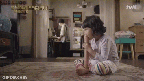 A Little Girl Sitting On A Rug With A Tvn Logo On The Wall Behind Her GIF