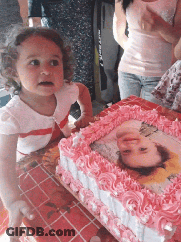 A Little Girl Stands In Front Of A Cake With A Picture Of A Girl On It GIF