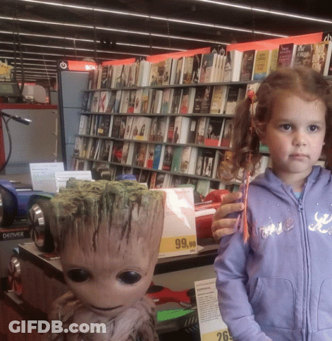 A Little Girl Stands Next To A Statue Of Groot In A Book Store GIF