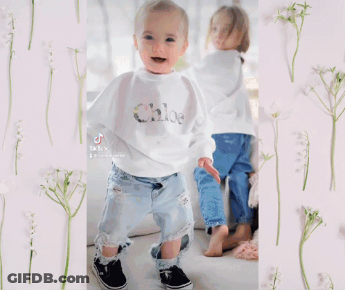 A Little Girl Wearing A Bell Sleeve Top And Ripped Jeans Is Standing In A Pile Of Leaves And Flowers GIF