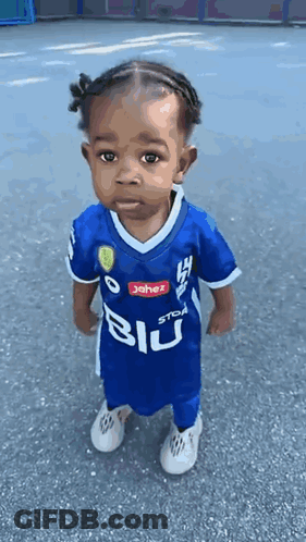 A Little Girl Wearing A Blue Soccer Jersey Is Standing On The Street . GIF