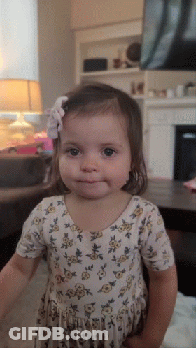 A Little Girl Wearing A Floral Dress With A Bow In Her Hair GIF