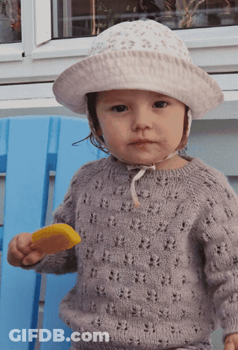 A Little Girl Wearing A Hat And Sweater Is Holding An Ice Cream Bar GIF