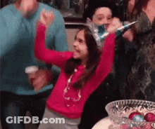 A Little Girl Wearing A Party Hat Is Dancing With Her Arms In The Air At A Party . GIF