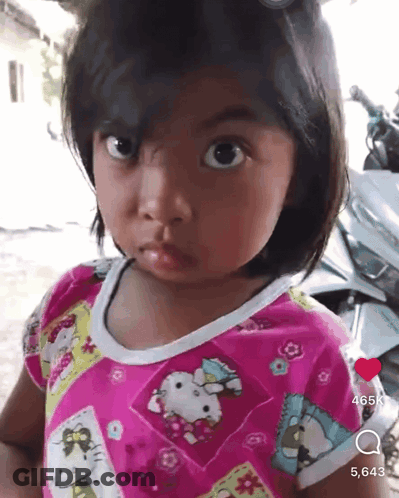 A Little Girl Wearing A Pink Hello Kitty Shirt Is Looking At The Camera GIF