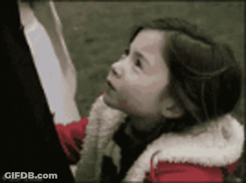 A Little Girl Wearing A Red And White Jacket Looks Up At Something GIF