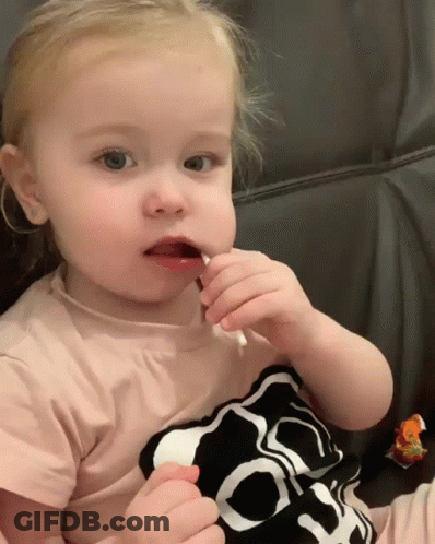 A Little Girl Wearing A Shirt With A Skull On It Eating A Lollipop GIF