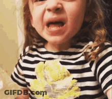 A Little Girl Wearing A Striped Shirt With A Yellow Flower On It Is Making A Funny Face . GIF