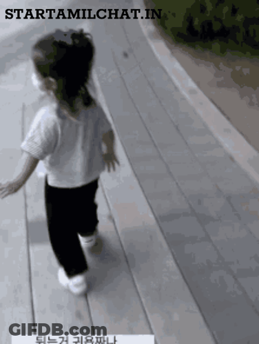 A Little Girl Wearing A White Shirt And Black Pants Is Walking Down A Wooden Walkway GIF