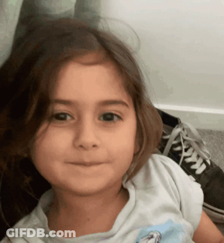 A Little Girl Wearing A White Shirt With A Picture Of A Horse On It Looks At The Camera GIF