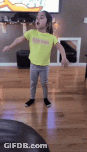 A Little Girl Wearing A Yellow Reebok Shirt Is Dancing In A Living Room GIF