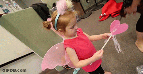 A Little Girl Wearing Fairy Wings And A Headband Holds A Pink Wand GIF
