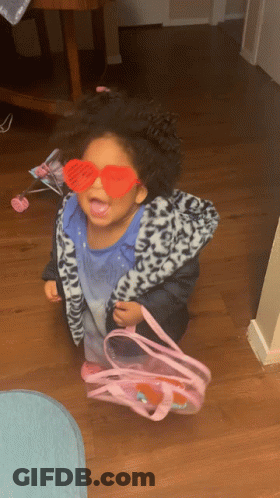 A Little Girl Wearing Heart Shaped Sunglasses And Holding A Pink Bag GIF