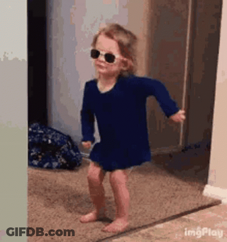 A Little Girl Wearing Sunglasses And A Blue Dress Is Dancing In A Hallway . GIF