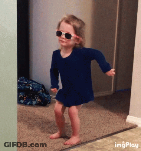 A Little Girl Wearing Sunglasses And A Blue Dress Is Dancing In A Hallway .. GIF
