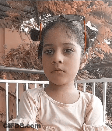 A Little Girl Wearing Sunglasses And Pigtails Is Looking At The Camera GIF