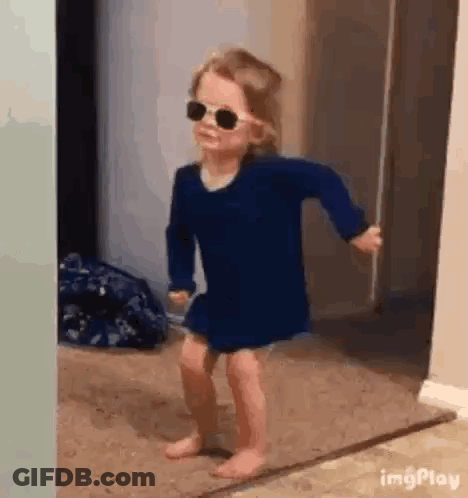 A Little Girl Wearing Sunglasses Is Dancing In A Hallway . GIF