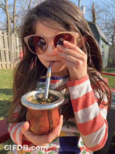 A Little Girl Wearing Sunglasses Is Drinking From A Cup GIF
