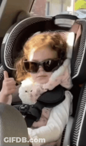 A Little Girl Wearing Sunglasses Is Sitting In A Car Seat GIF