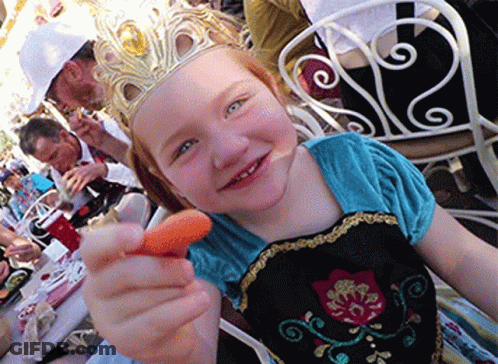 A Little Girl With A Crown On Her Head Is Holding A Carrot GIF