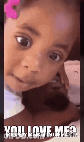 A Little Girl With A Pink Flower In Her Hair Is Looking At The Camera With A Caption That Says You Love Me ? GIF