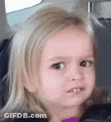 A Little Girl With Blonde Hair Is Making A Funny Face In A Car Seat . GIF