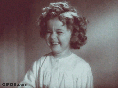 A Little Girl With Curly Hair And A White Shirt Is Smiling GIF